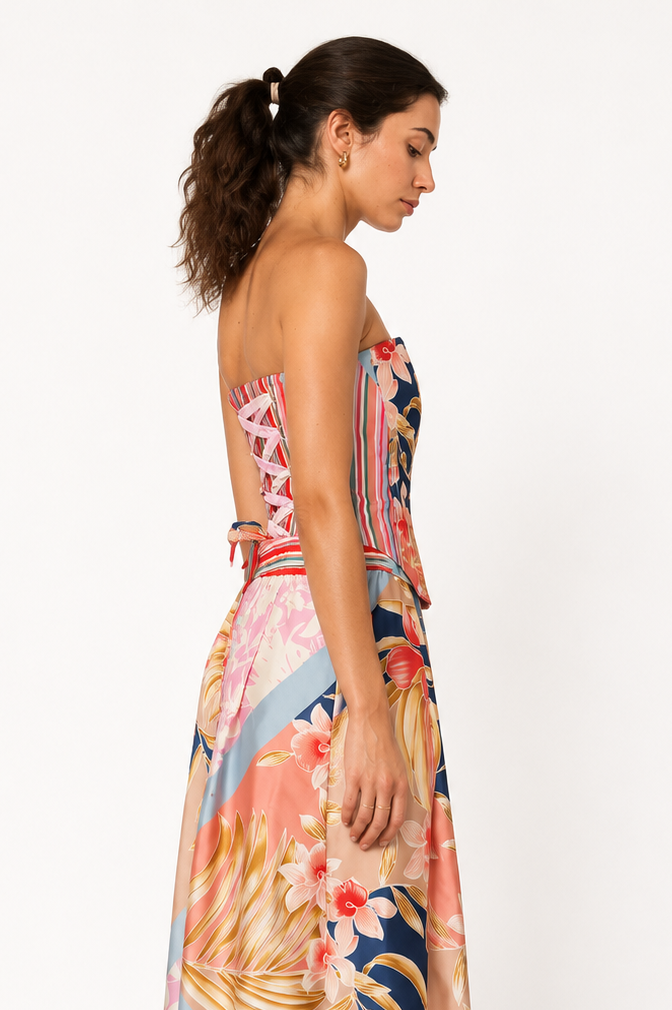 A woman modeling a strapless maxi dress with a colorful tropical floral and striped print, shown from a side-back angle against a plain white studio background.