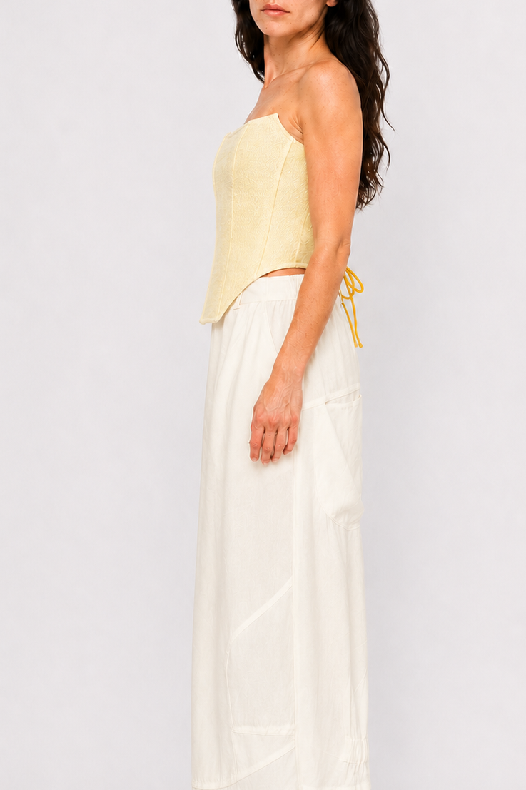 A woman modeling a pale yellow strapless tube top and white wide-leg pants against a light gray studio background.