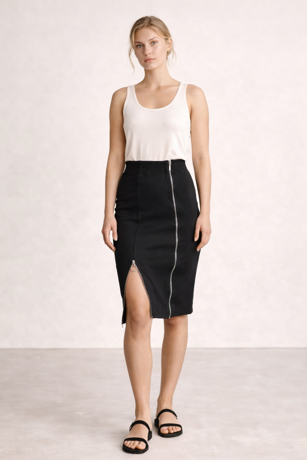 Woman wearing a white sleeveless top and black skirt with a zipper on a plain background