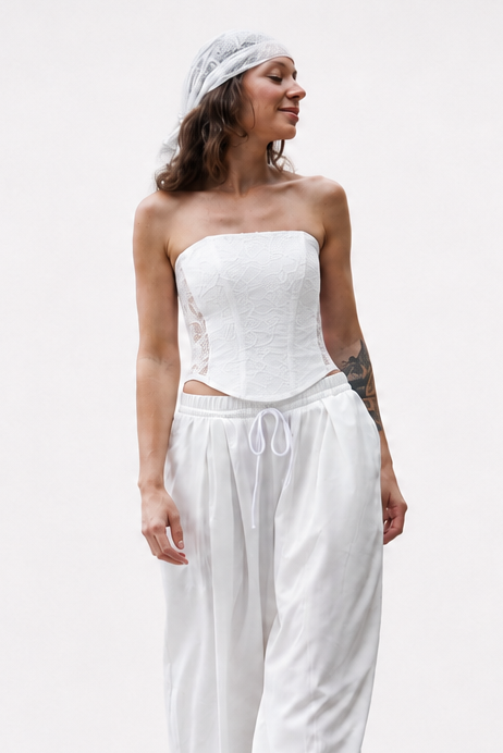 A woman modeling a white strapless corset top with a corset-style waist and matching loose white drawstring pants, standing against a plain white studio background.


